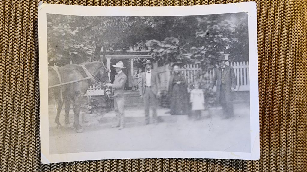 Mid to late 1800s photo of a group of people near horses hitched to a wagon. 